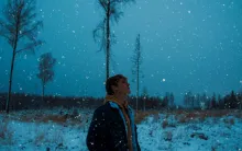 a man standing outside in the snow with snowflakes falling against a darkened sky