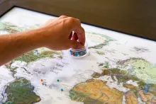 a hand reaching into a plastic container of colorful pins sitting atop a world map