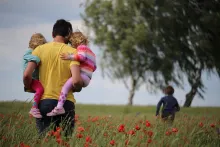 A father walking in field carrying two daughters.