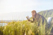 A man reading a Bible sitting on a park bench.
