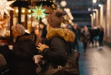 A woman standing in line surrounded by people and Christmas lights.