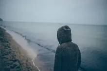 A person wearing a hoodie looking at the waves of the ocean.