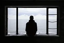 A teen sitting in abandoned window frame of an old house.