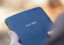 A person holding a blue covered Bible.