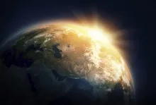 A sun burst shining around the side of the earth from space.