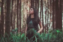 A young woman staring up while standing in tall grass near trees.