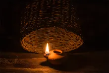 A basket almost covering the light of a small oil lamp.