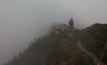 A person hiking on a narrow mountain path surrounded by fog.