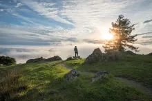 A man standing on top of hill with the sun in the background.