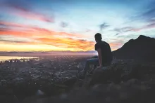 A young man sitting on a rock looking at the cityscape below.