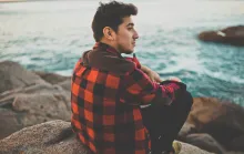 A young man sitting on a rock looking out over the water.