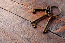 Three old skeleton keys laying on an old wood table.