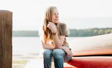 A young woman sitting on the edge of kayak that is on the shore.