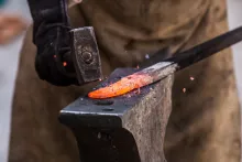 Close-up photo of a hammer striking a heated piece of metal.