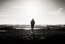 A silhouette of a person walking towards water.
