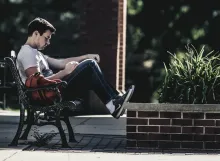 A man sitting on a park bench reading.