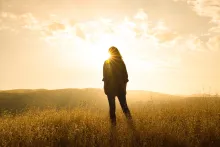 A woman standing in front of sun rays in an open field.