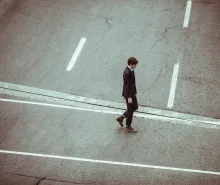 A young man in a suit walking across a road.
