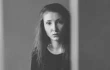 A young woman looking from behind an edge of a wall.