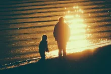 A dad and his children walking on the beach as the sun is setting.