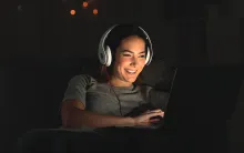 A girl wearing headphones while watching the screen of a laptop.
