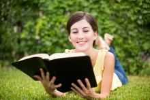 A woman reading a Bible while laying on a grassy field.