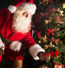 Santa Claus putting Christmas gifts by a tree.