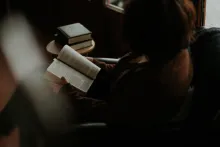 A sitting in a chair reading a Bible.