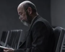 A man sitting in hall with chairs looking at notes.