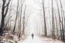 A person walking on a path in the woods covered with snow.