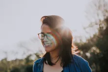 A young woman smiling with sun rays behind her head.