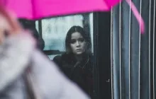 A woman looking out a window when it is raining.