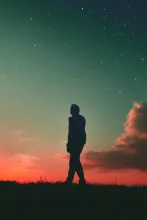 Silhouetted person against a dramatic, colorful sunset sky, with the person's silhouette filled with a different background, of a starry sky.