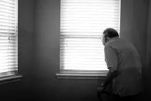 An elderly man looking out a window.