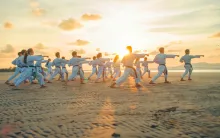 A group of people practicing martial arts moves on a beach.