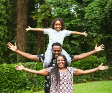 a man, woman, and child standing outdoors with outstretched arms and smiles