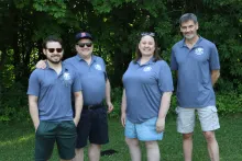 four people standing outdoors with matching camp shirts