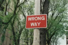 a wrong way sign on a post with green trees and buildings in the background