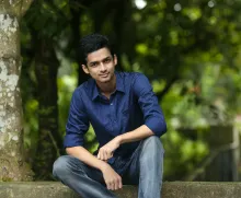 a young man sitting on a concrete ledge with trees in the background