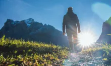 A person walking up a path with the sun in front of them.