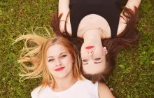 two women smiling and lying on the grass beside one another