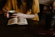 a woman holding a coffee cup beside an open Bible