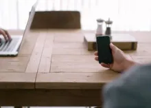 Sitting at table working on laptop and viewing smartphone.