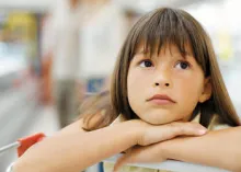 A young girl leaning on a shopping cart.