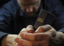 A man praying and holding the Holy Bible.