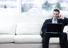 Man sitting on a couch with a laptop and talking on phone.