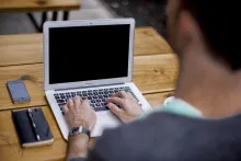 A man typing on a laptop while sitting a desk.