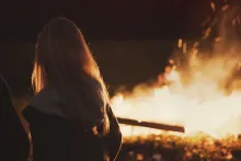 A woman standing by a bonfire.