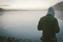 A young man standing by a lake.