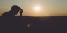 A young man sitting with head resting on tips of his finger. The sun is setting in the background.
